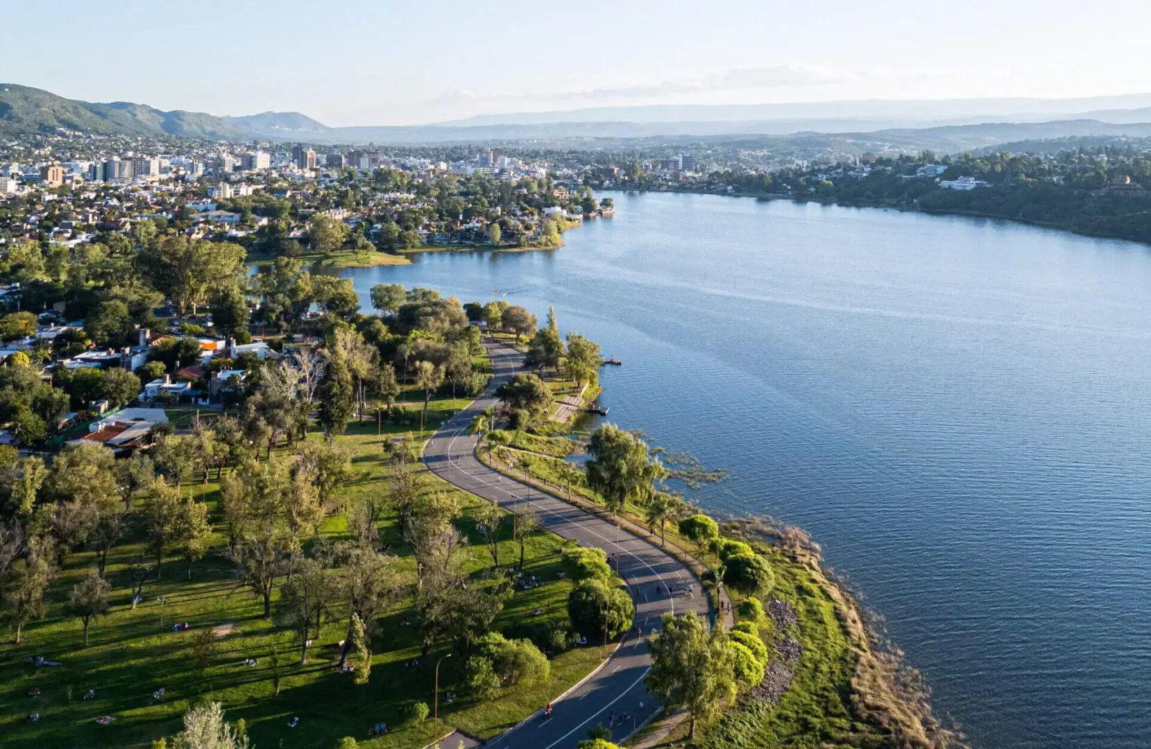 Vista aérea de la Costanera de Villa Carlos Paz y el Lago San Roque en Córdoba, Argentina, rodeados de vegetación y sierras.